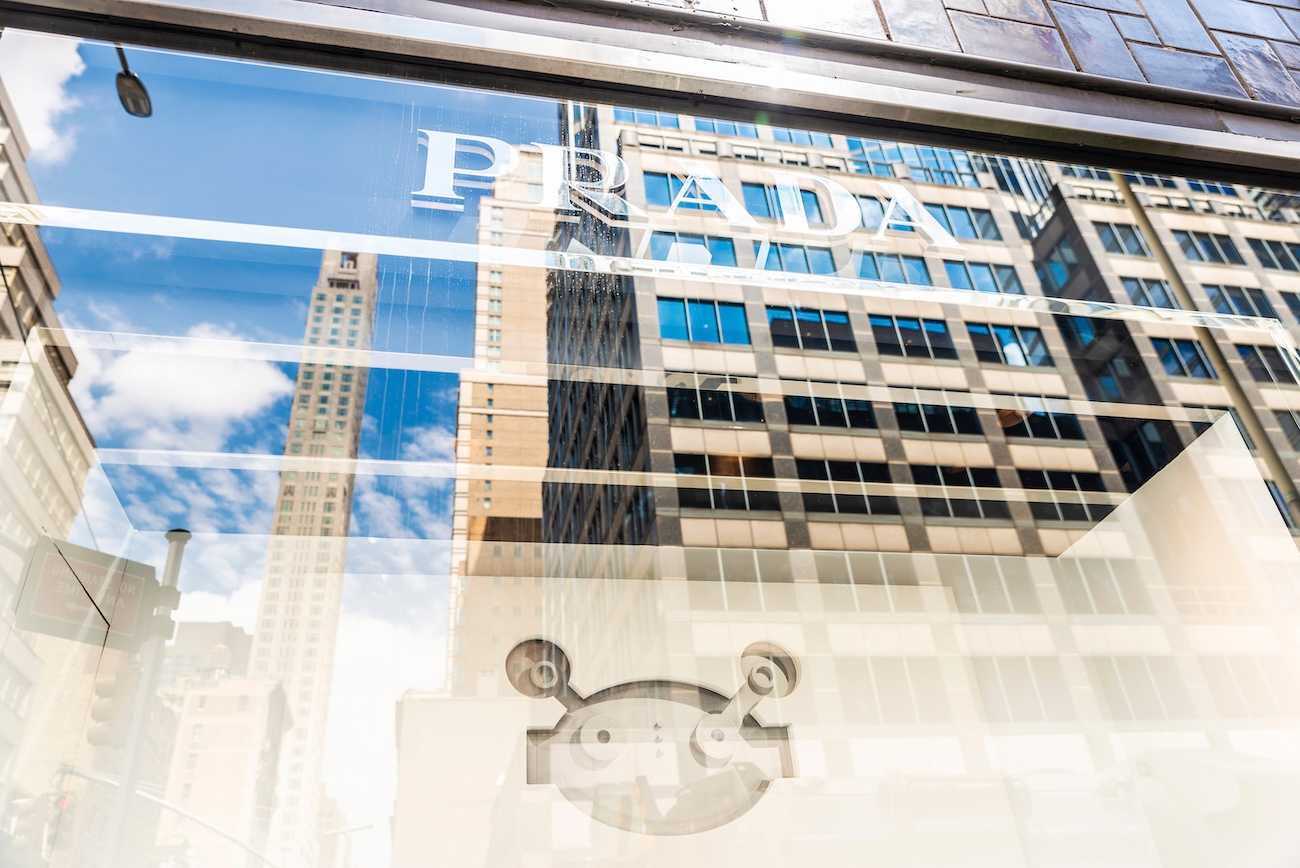 Prada wordmark on a glass window with the reflection of high rise buildings